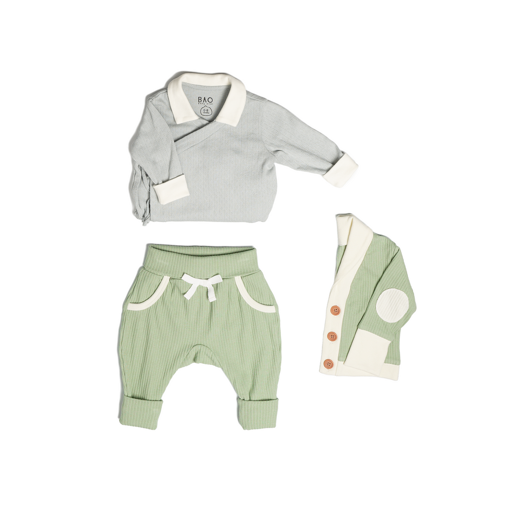 The newborn essentials bundle, consisting of a kimono bodysuit in a gentle blue (butterfly pea) pointelle patterned cotton, paired with lounge pants in matcha and ribbed cotton and a cardigan in matcha ribbed cotton.
