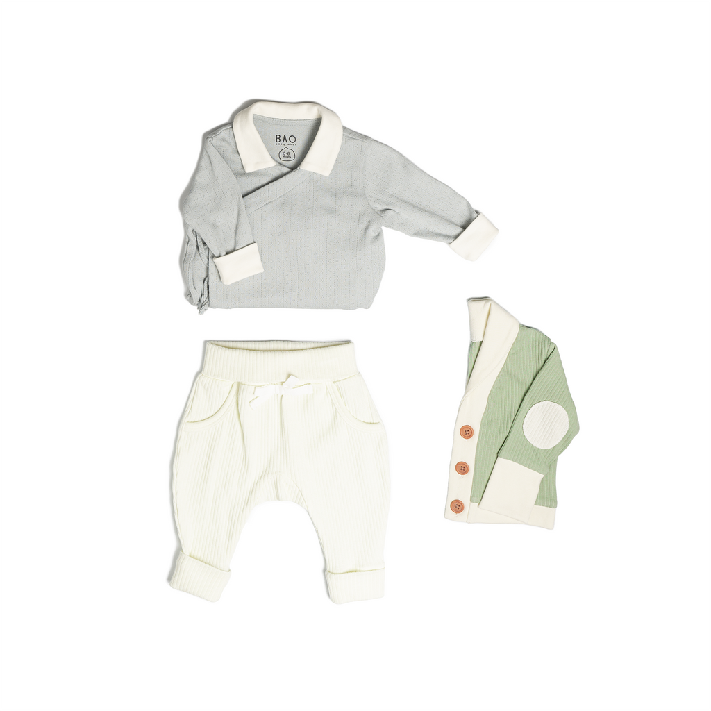 The newborn essentials bundle, consisting of a kimono bodysuit in a gentle blue (butterfly pea) pointelle patterned cotton, paired with lounge pants in vanilla and ribbed cotton and a cardigan in matcha ribbed cotton.