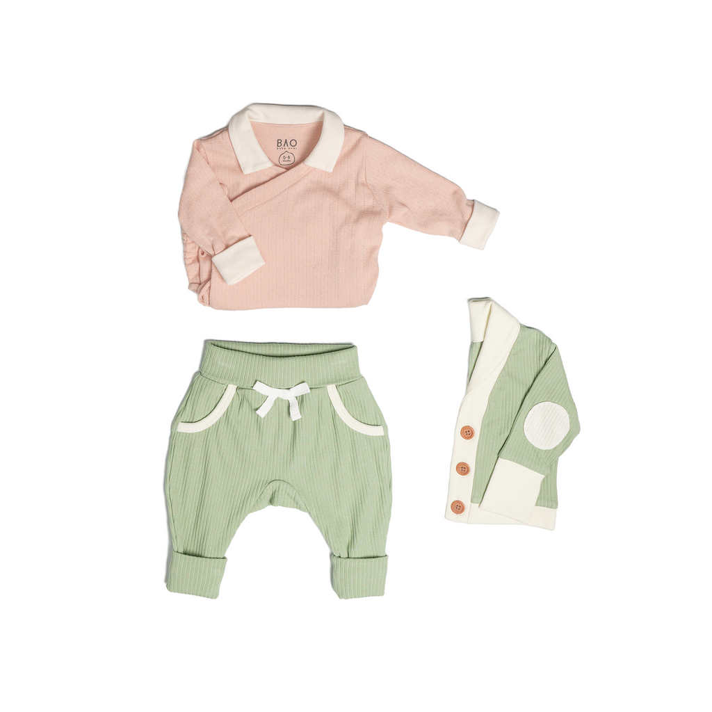 The newborn essentials bundle, consisting of a kimono bodysuit in a peach pointelle patterned cotton, paired with lounge pants in matcha and ribbed cotton and a cardigan in matcha ribbed cotton.
