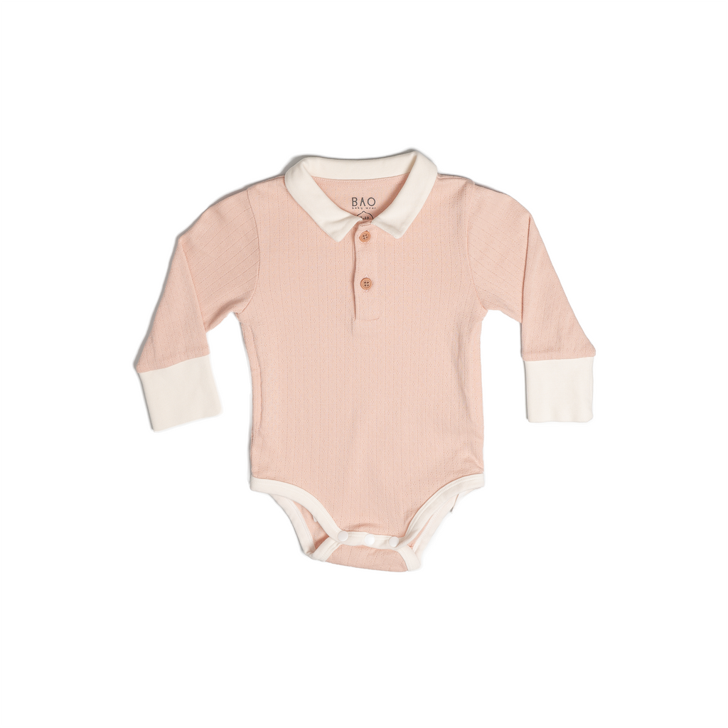A long sleeve bodysuit, complete with a 2 buttons on the collar. In a gentle salmon pink (peach) pointelle patterned cotton. Shown in its large setting.
