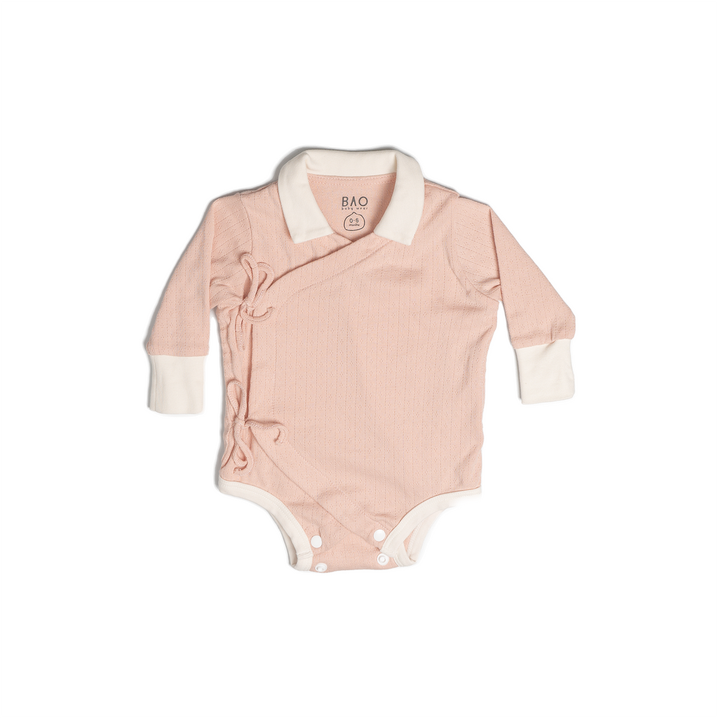 A long sleeve kimono opening bodysuit with a vanilla collar and sleeve cuffs. Made from pointelle patterned cotton in a gentle salmon pink (peach). Shown in its large setting.