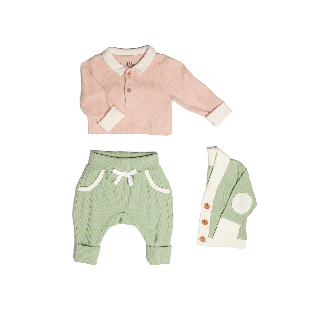 The toddler essentials bundle, consisting of a collared bodysuit in peach pointelle patterned cotton, paired with lounge pants in matcha and ribbed cotton and a cardigan in matcha ribbed cotton.