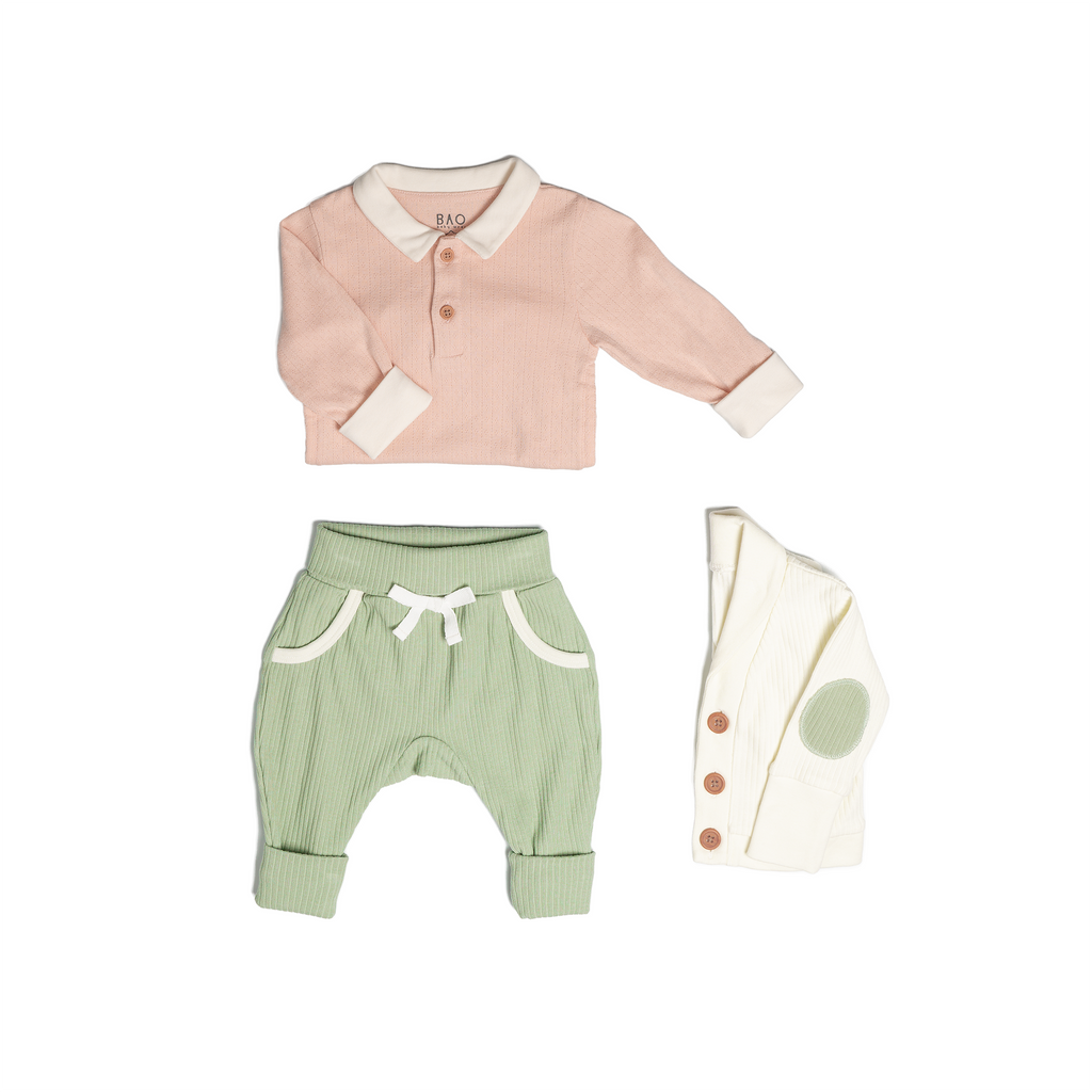 The toddler essentials bundle, consisting of a collared bodysuit in peach pointelle patterned cotton, paired with lounge pants in matcha and ribbed cotton and a cardigan in vanilla ribbed cotton.