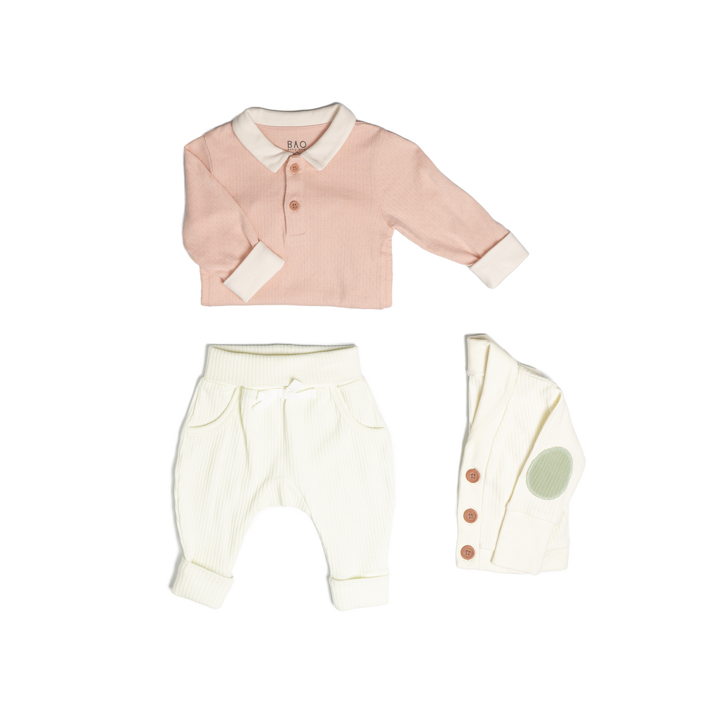 The toddler essentials bundle, consisting of a collared bodysuit in peach pointelle patterned cotton, paired with lounge pants in vanilla and ribbed cotton and a cardigan in vanilla ribbed cotton.